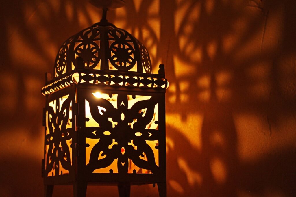 A traditional Moroccan lamb tagine served in a decorative clay pot, placed on a wooden table inside a riad in Marrakech. The riad features intricate mosaic tiles, carved wooden furniture, and soft lighting, showcasing the authentic Moroccan decor.