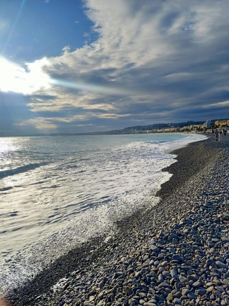 A serene beach in Nice, France, with turquoise Mediterranean waters, smooth pebbles, and a view of the iconic Promenade des Anglais.