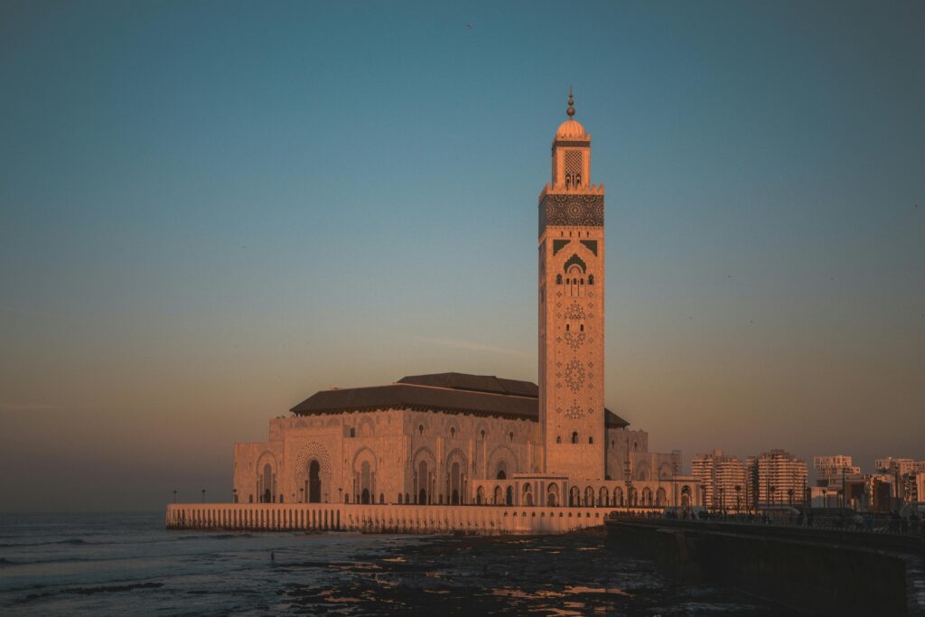 The majestic Hassan II Mosque in Casablanca with its towering minaret, overlooking the Atlantic Ocean, under a clear blue sky.