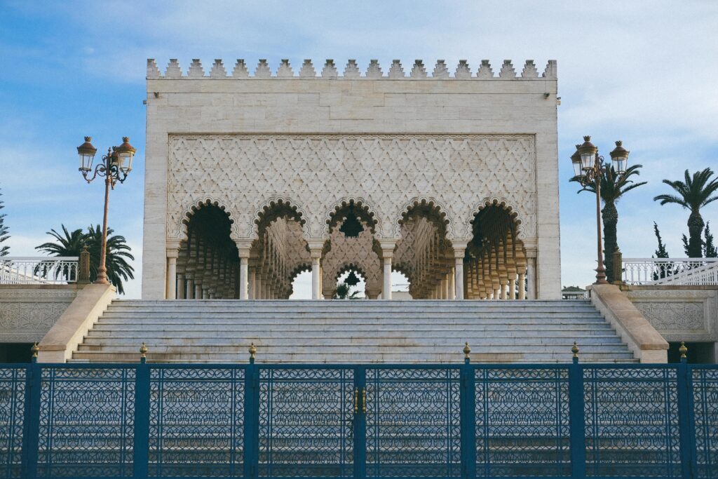 A scenic view of the Hassan Tower in Rabat, with its historic minaret standing tall against a clear blue sky, surrounded by lush green gardens and the tranquil atmosphere of the city