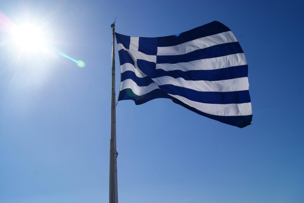 The flag of Greece, featuring nine horizontal stripes of blue and white, with a white cross on a blue square in the top left corner, symbolizing the sky, sea, and Greek Orthodox faith.