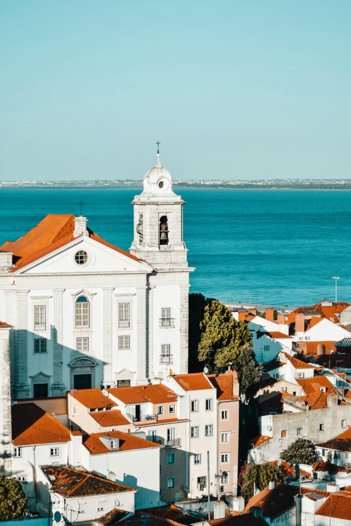 Panoramic view of Lisbon, Portugal, showcasing colorful buildings, the Tagus River, and iconic red rooftops under a clear blue sky.